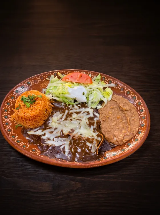 Enchiladas under dark sauce and melted cheese with rice, refried beans, lettuce and tomato.