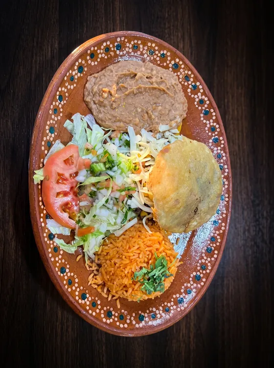 A golden stuffed round of fried masa with lettuce, tomato and cheese, beside rice and refried beans.