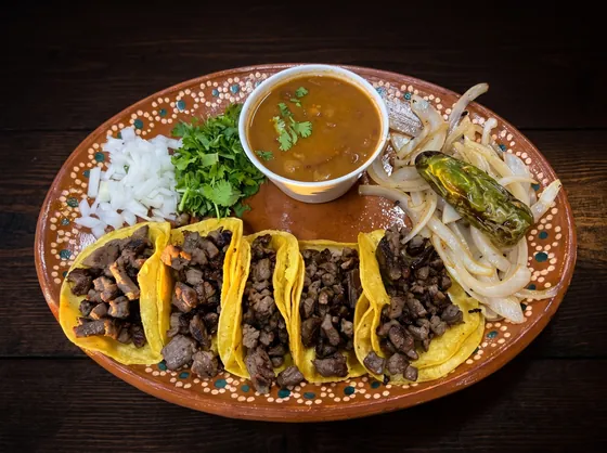 Five soft corn tacos of chopped grilled beef with a cup of consommé, onion, cilantro, grilled onions and a charred jalapeño.