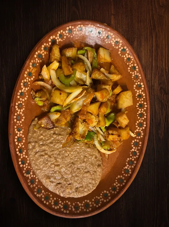 Fried potato cubes cooked with onion and green pepper, beside refried beans.
