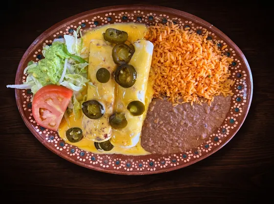 Enchiladas under yellow cheese sauce and sliced jalapeños, with rice, refried beans, lettuce, guacamole and tomato.