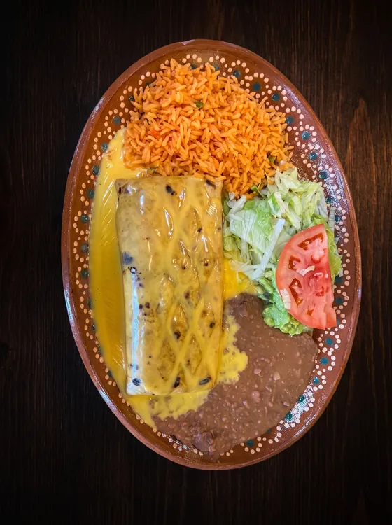 A burrito under a lattice of yellow cheese sauce, with rice, refried beans, lettuce and tomato.