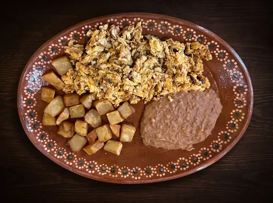 Shredded dried beef scrambled with egg, beside fried potato cubes and refried beans.