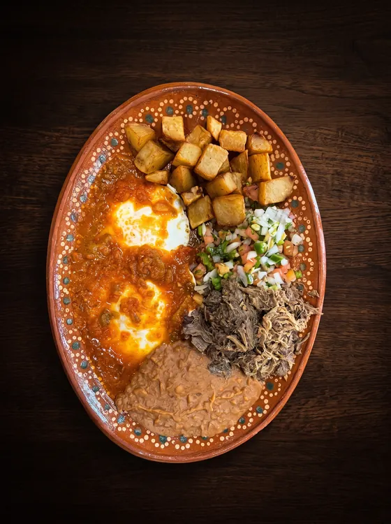 Eggs under red sauce with shredded beef, pico de gallo, fried potato cubes and refried beans.