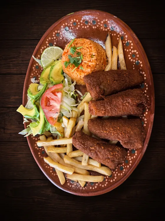 Long breaded fish strips with french fries, rice, avocado, lettuce, tomato and a lime wedge.