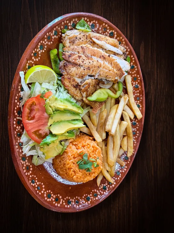A grilled fish fillet with french fries, rice, sliced avocado, lettuce, tomato and lime.