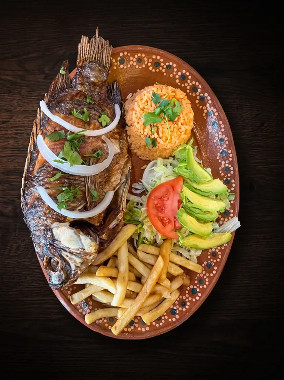 A whole fried fish topped with onion rings, with rice, french fries, avocado, lettuce and tomato.