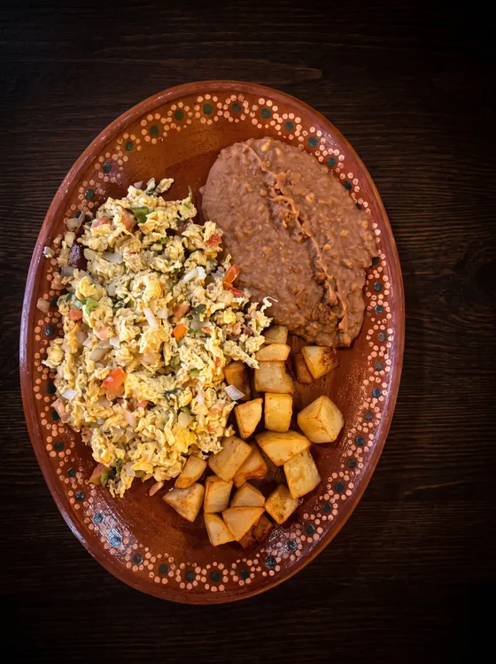 Scrambled eggs with tomato, onion and pepper, beside fried potato cubes and refried beans.