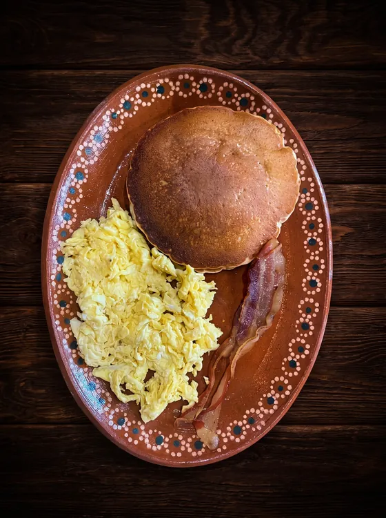 Scrambled eggs with a thick golden round of fried masa and a strip of bacon.