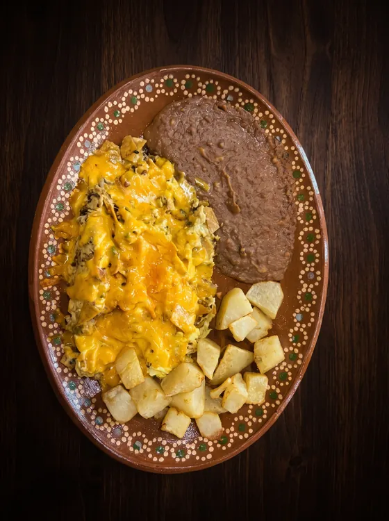 Scrambled eggs under melted cheese, beside fried potato cubes and refried beans.