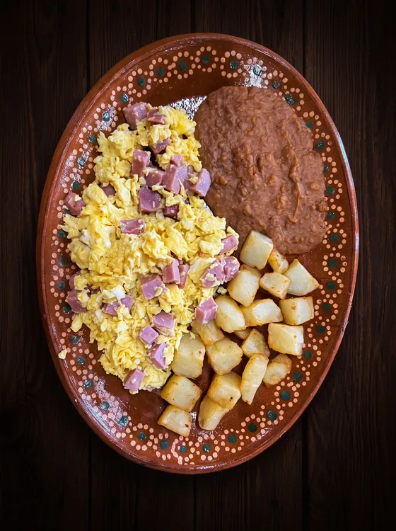 Scrambled eggs with diced ham, beside fried potato cubes and refried beans.