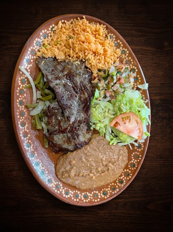 A thin grilled steak over grilled onion and cactus strips, with rice, refried beans, guacamole, pico de gallo and tomato.