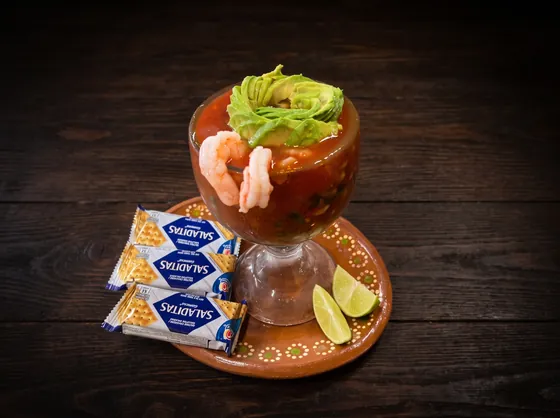 A second view: shrimp and avocado in red sauce in a footed glass, with lime wedges and three packets of saltine crackers.