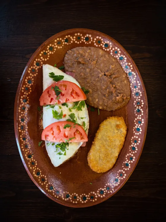 A folded omelette topped with tomato slices and cilantro, beside refried beans and a hash brown.