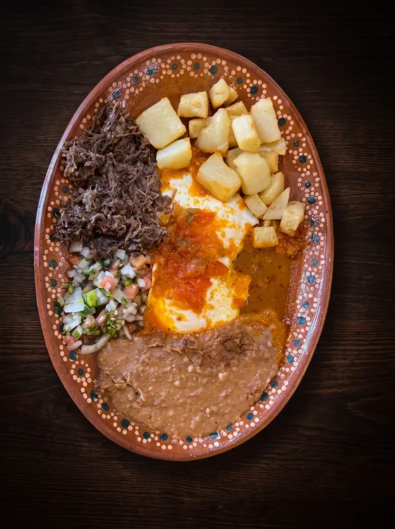 Eggs under red sauce with shredded beef, fried potato cubes, pico de gallo and refried beans.