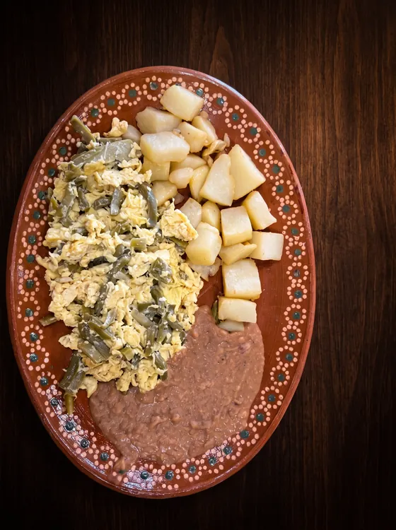 Scrambled eggs with strips of cactus, beside potato cubes and refried beans.