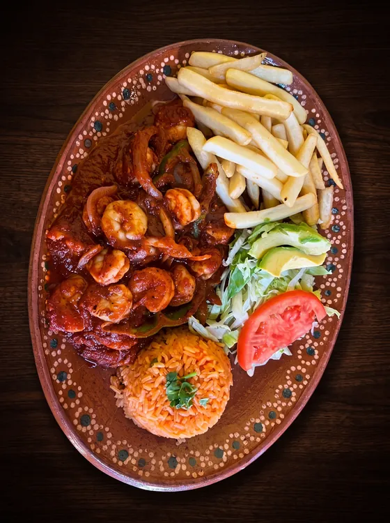 Shrimp in a glossy red sauce with onion, beside french fries, rice, avocado, lettuce and tomato.