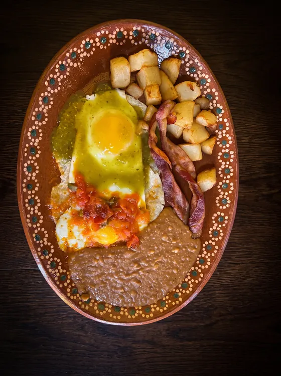 Eggs under green and red salsa with bacon, fried potato cubes and refried beans.