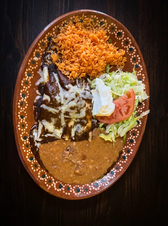 Enchiladas under dark sauce and melted white cheese, with rice, refried beans, lettuce, sour cream and tomato.