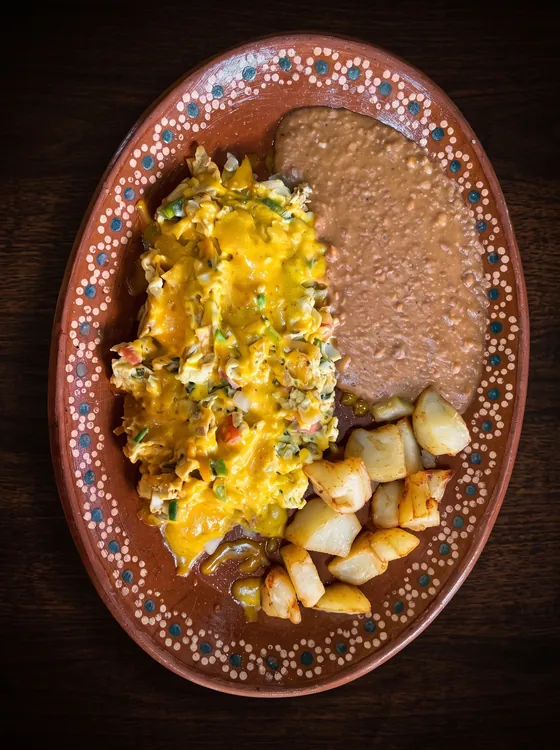 Scrambled eggs with melted cheese and green pepper, beside fried potato cubes and refried beans.