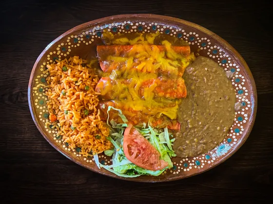 Enchiladas under melted yellow cheese and red sauce, with rice, refried beans, lettuce and tomato.