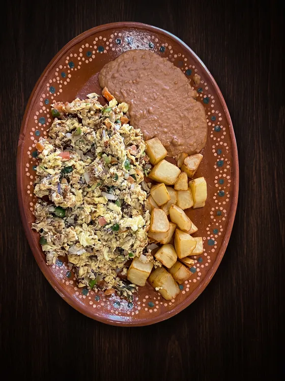 Shredded dried beef scrambled with egg, onion and pepper, beside fried potato cubes and refried beans.