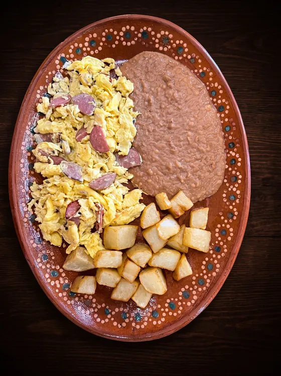 Scrambled eggs with pieces of ham, beside fried potato cubes and refried beans.