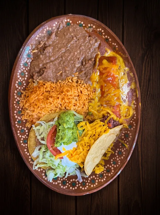 A crisp taco, an enchilada and a flat tostada with guacamole, lettuce and cheese, beside rice and refried beans.