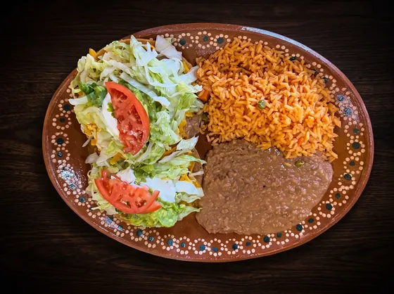 Two flat crisp tortillas piled with lettuce and tomato, beside rice and refried beans.