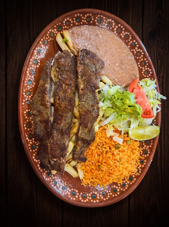 Long grilled strips of meat over french fries, with refried beans, rice, guacamole, lettuce, tomato and lime.