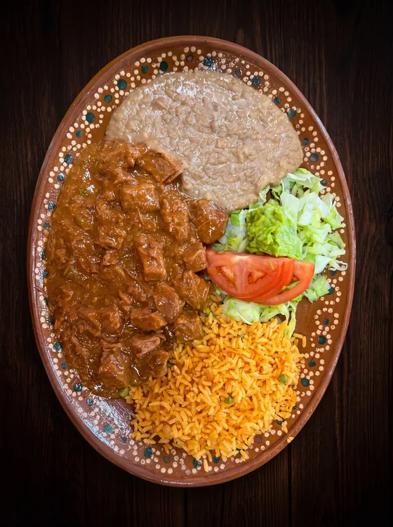 Chunks of beef stewed in a brown gravy, with refried beans, rice, guacamole, lettuce and tomato.