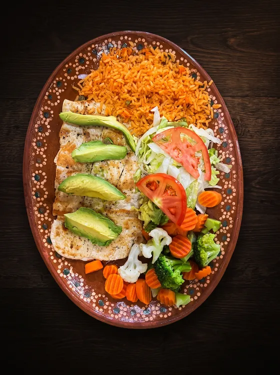 Grilled chicken topped with avocado slices, with steamed broccoli, carrot and cauliflower, rice, lettuce and tomato.