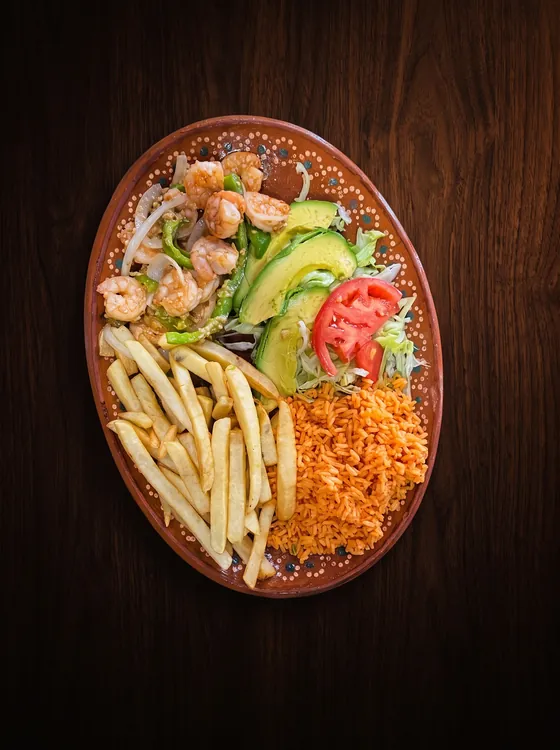 Shrimp with onion beside sliced avocado, tomato, lettuce, french fries and rice.