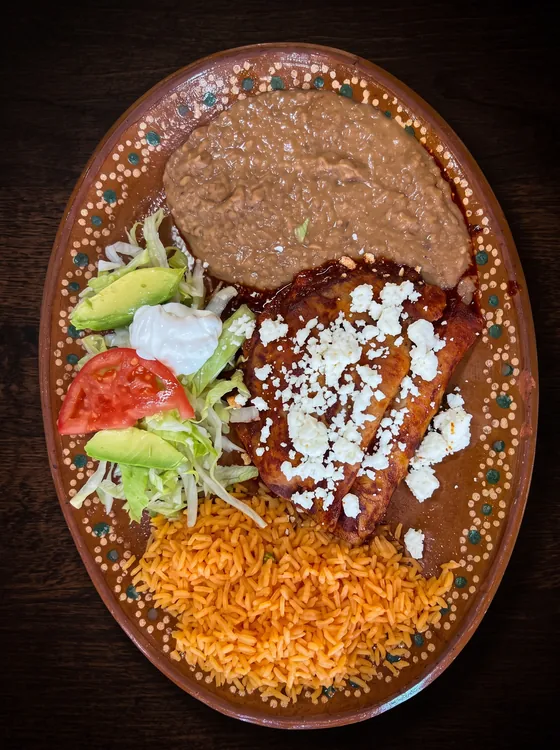 Enchiladas under red sauce and crumbled white cheese, with refried beans, rice, avocado, sour cream, lettuce and tomato.