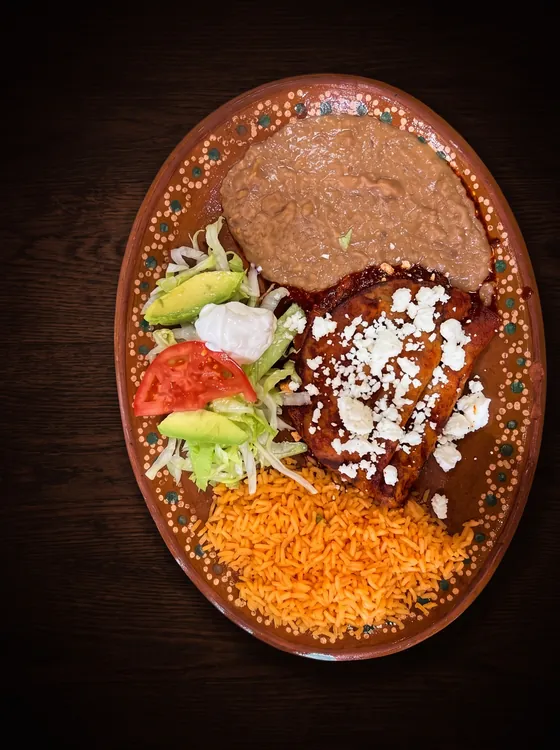 A second view: enchiladas under red sauce and crumbled white cheese, with refried beans, rice, avocado and tomato.