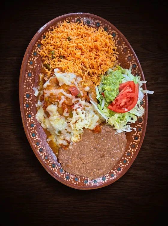 A battered pepper under sauce and melted cheese, with rice, refried beans, lettuce, guacamole and tomato.