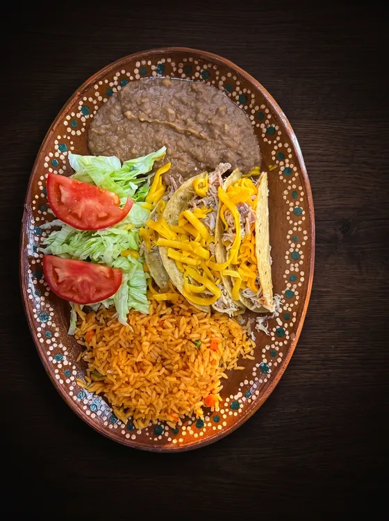 Crisp tacos with shredded cheese beside lettuce, tomato, rice and refried beans.