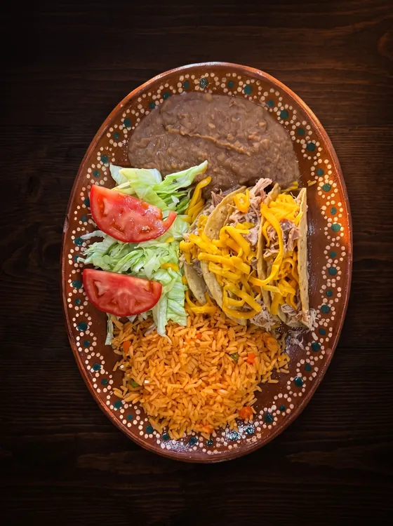Crisp tacos topped with lettuce, tomato and shredded cheese, with rice and refried beans.