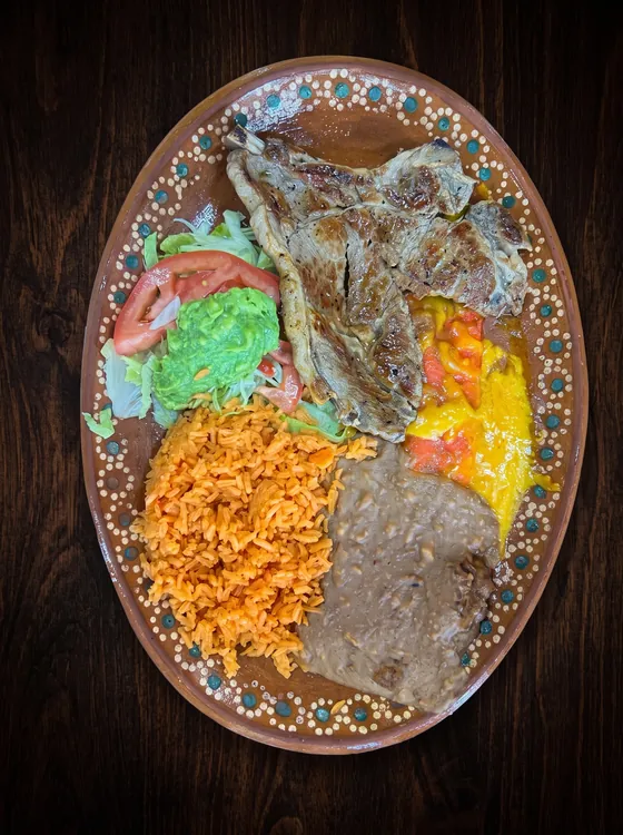 Grilled bone-in chops with rice, refried beans, lettuce, guacamole, tomato and a spoon of yellow cheese.