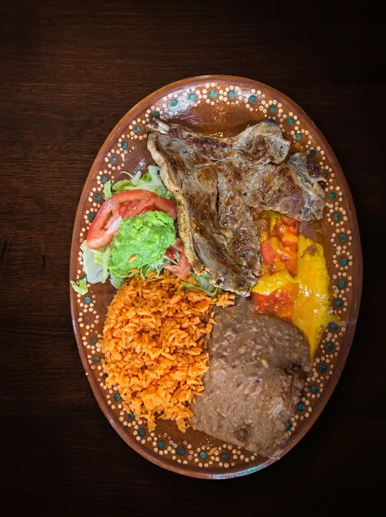 A second view: grilled bone-in chops with rice, refried beans, guacamole, lettuce and tomato.