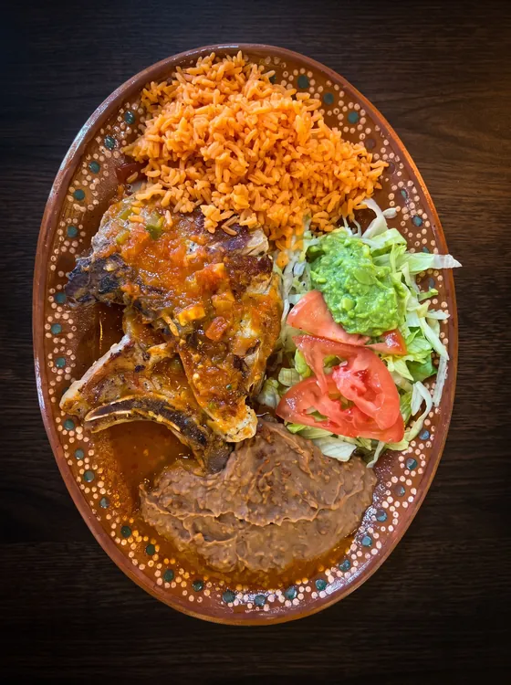 Bone-in chops under red sauce with rice, refried beans, lettuce, guacamole and tomato.