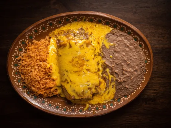 A burrito smothered in yellow cheese sauce, between rice and refried beans.