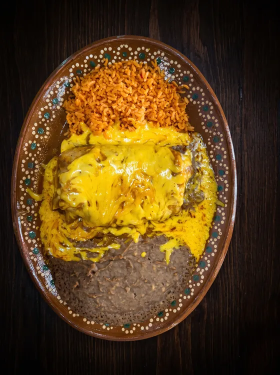 A burrito under melted yellow cheese, with rice above and refried beans below.