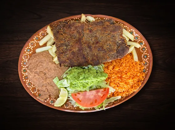 A flat breaded cutlet over french fries, with refried beans, rice, guacamole, lettuce, tomato and lime.