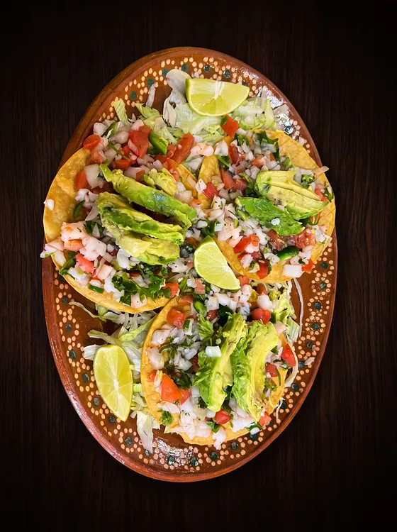 Crisp flat tortillas heaped with shrimp, pico de gallo and avocado slices, with lime wedges.