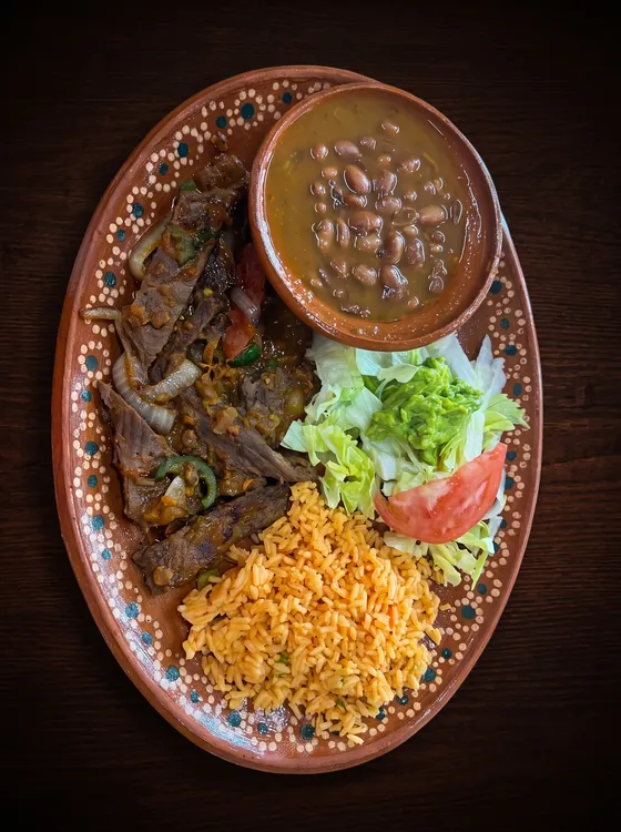 Grilled beef with onion and pepper, a cup of whole beans in broth, rice, guacamole, lettuce and tomato.