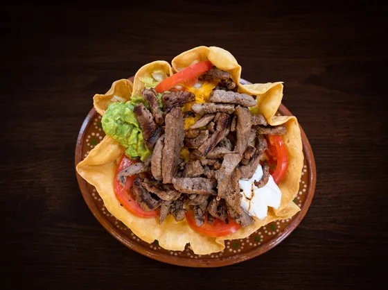 A crisp tortilla bowl filled with grilled beef strips, guacamole, sour cream, tomato and cheese.
