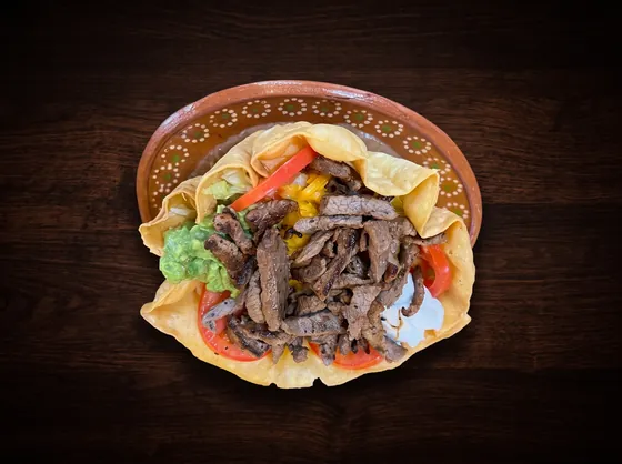 A second view: a crisp tortilla bowl filled with grilled beef strips, guacamole and sour cream.