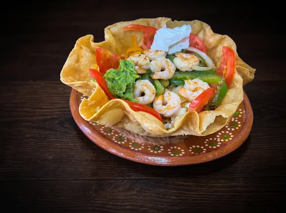 A crisp tortilla bowl filled with shrimp, peppers, guacamole, sour cream and tomato.